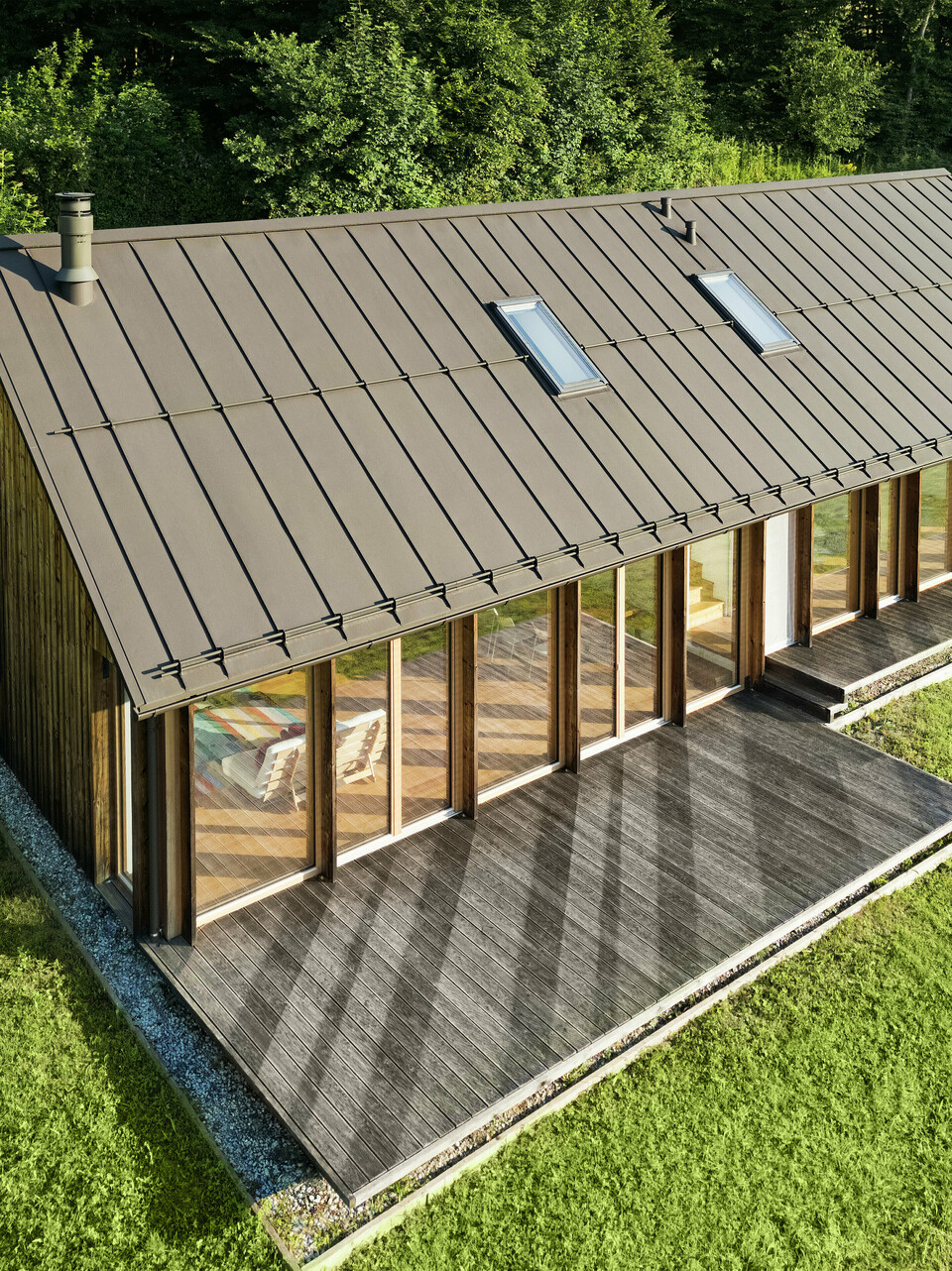 Modernes Holzhaus mit großzügiger Glasfassade und strapazierfähigem PREFALZ Aluminiumdach in P.10 Braun – ideal für Hanglagen wie in Vinje. Die hochwertige Dacheindeckung sorgt für maximale Wetterbeständigkeit, lange Lebensdauer und eine elegante Optik. Durch präzise Verlegung der Stehfalze und integrierte Dachfenster entsteht ein lichtdurchflutetes, nachhaltiges Wohnkonzept. Die Vogelperspektive zeigt die präzise Verarbeitung der Stehfalze aus Aluminium.