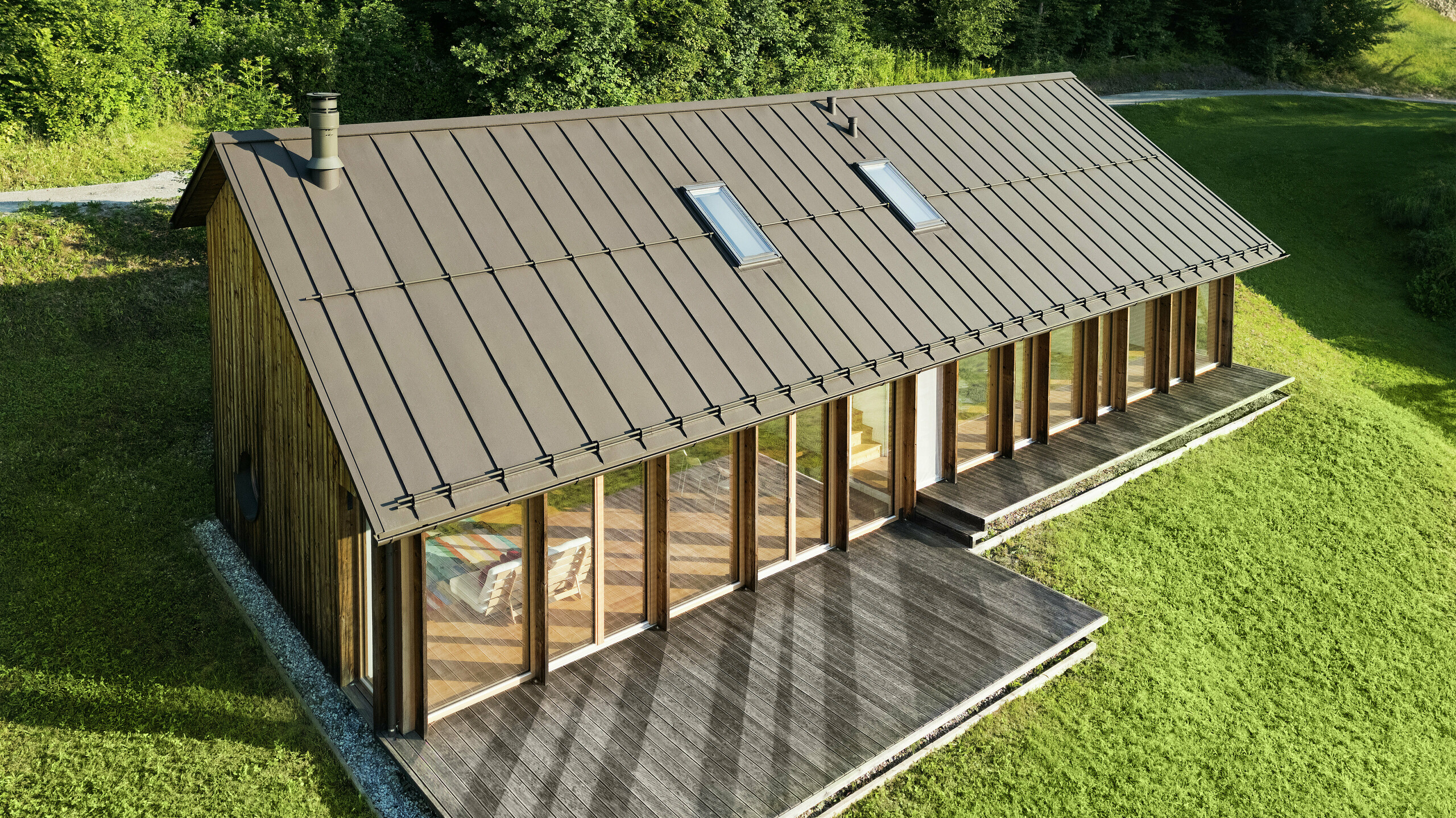 Modernes Holzhaus mit großzügiger Glasfassade und strapazierfähigem PREFALZ Aluminiumdach in P.10 Braun – ideal für Hanglagen wie in Vinje. Die hochwertige Dacheindeckung sorgt für maximale Wetterbeständigkeit, lange Lebensdauer und eine elegante Optik. Durch präzise Verlegung der Stehfalze und integrierte Dachfenster entsteht ein lichtdurchflutetes, nachhaltiges Wohnkonzept. Die Vogelperspektive zeigt die präzise Verarbeitung der Stehfalze aus Aluminium.