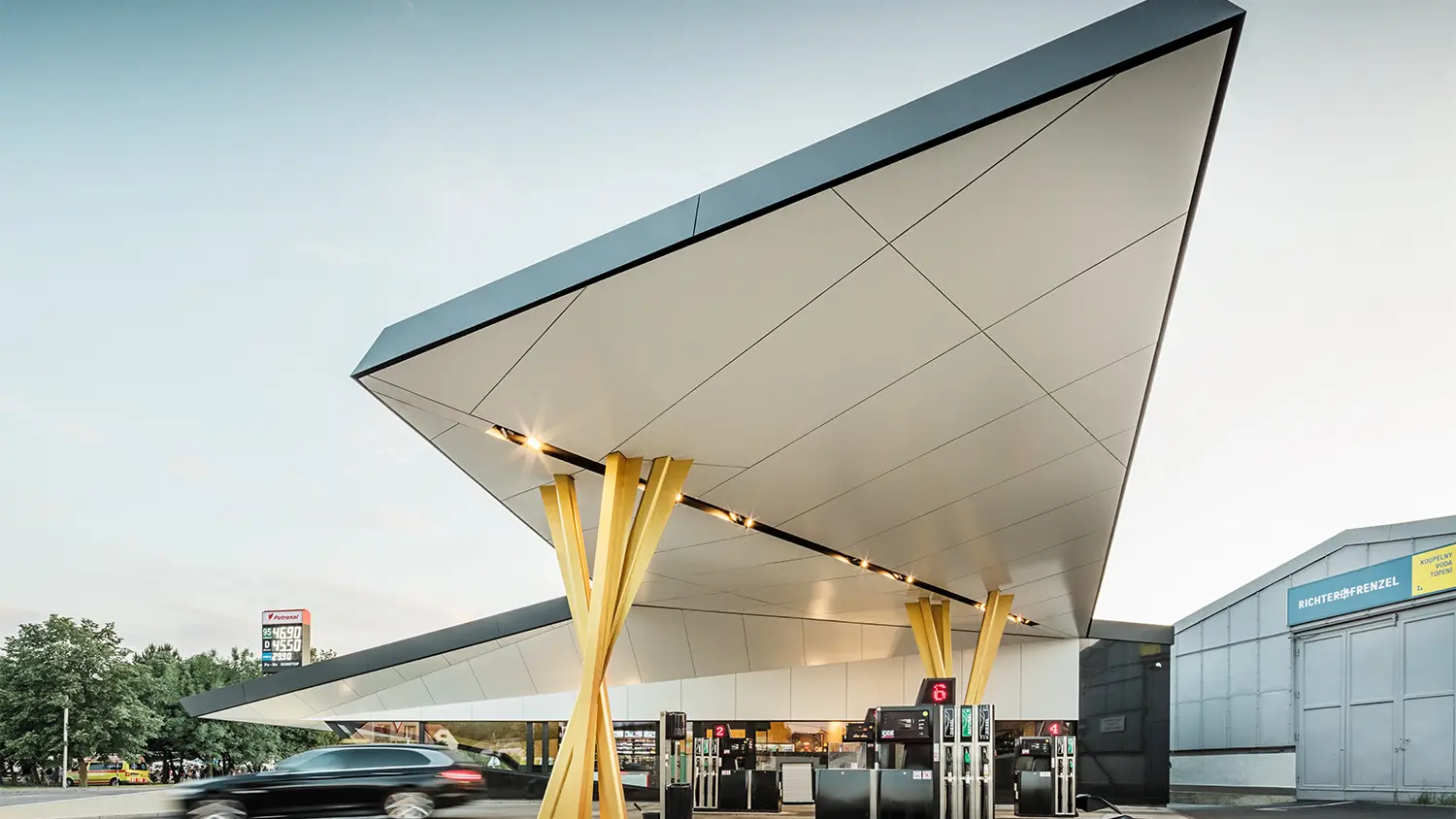 Side view of the petrol station with a bottom view of the roof, which rests on two groups of golden supports.