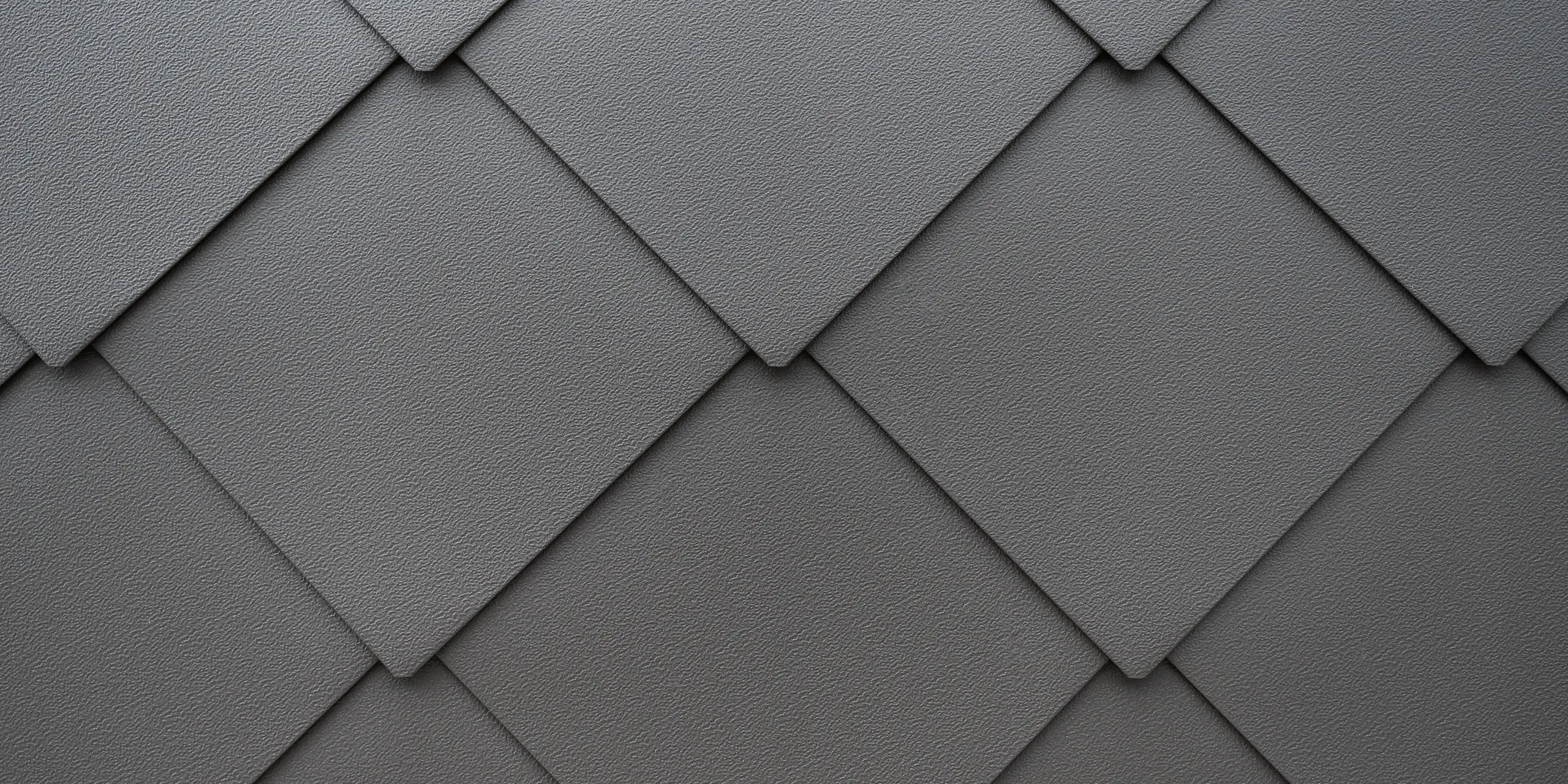 Detailaufnahme der texturierten Oberfläche eines PREFA Fassadensystems aus Aluminium. Die harmonische Anordnung der PREFA Wandrauten 44x44 erzeugt ein klares, geometrisches Muster, das Eleganz und moderne Architektur widerspiegelt, betont durch die subtile Farbgebung und die präzise Verarbeitung. Das widerstandsfähige Blech bietet dem Reihenhaus in Kaltern, Südtirol, Schutz vor winterlichen Bedingungen.