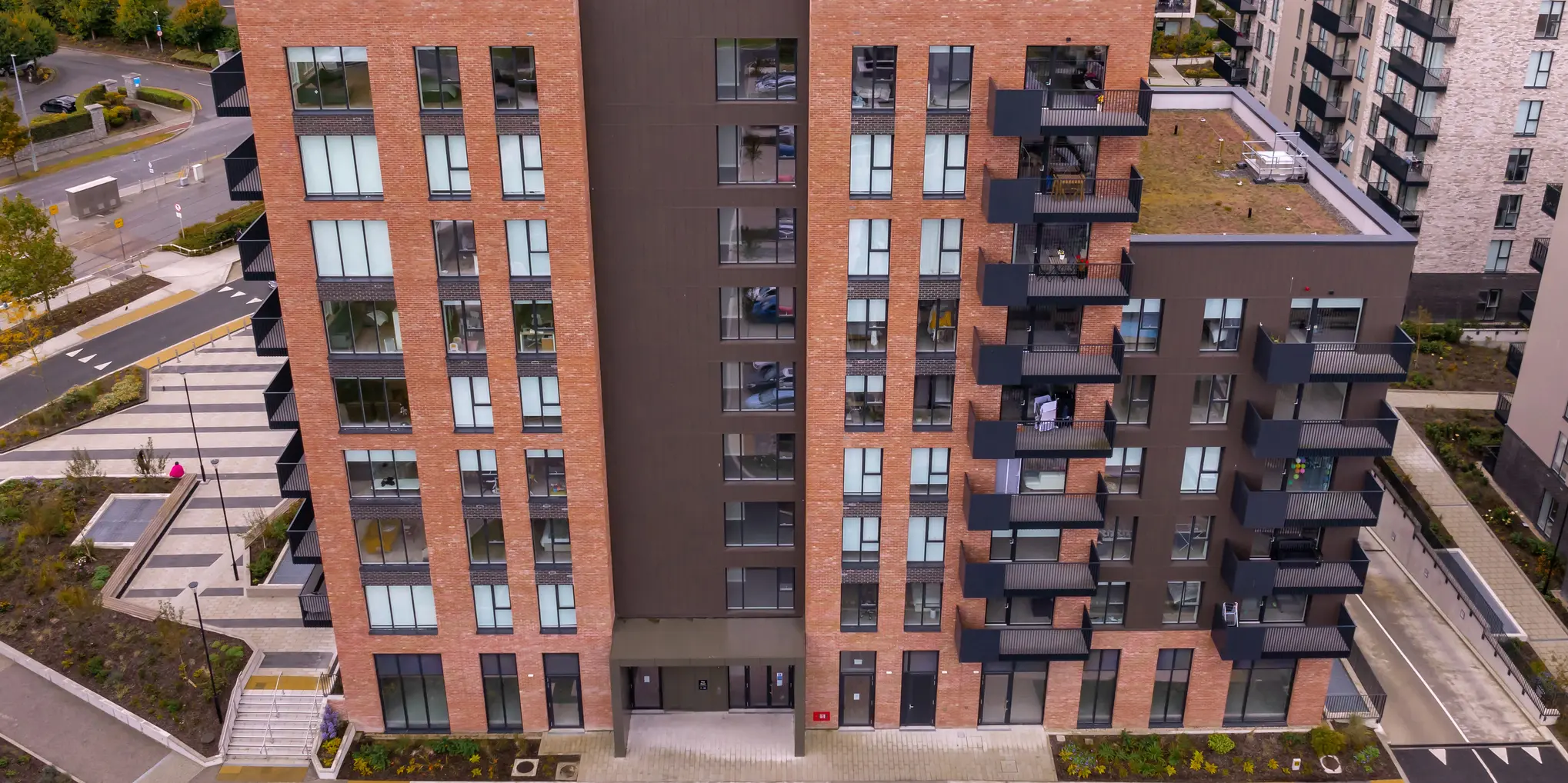 A bird's eye view of the Citywest Apartments in Dublin. The façade combination of traditional brick and 700 m² of PREFA sidings in P.10 brown blends harmoniously into the modern architecture and surroundings.  You can see the entrance area of the residential complex with well-tended green spaces around the building.