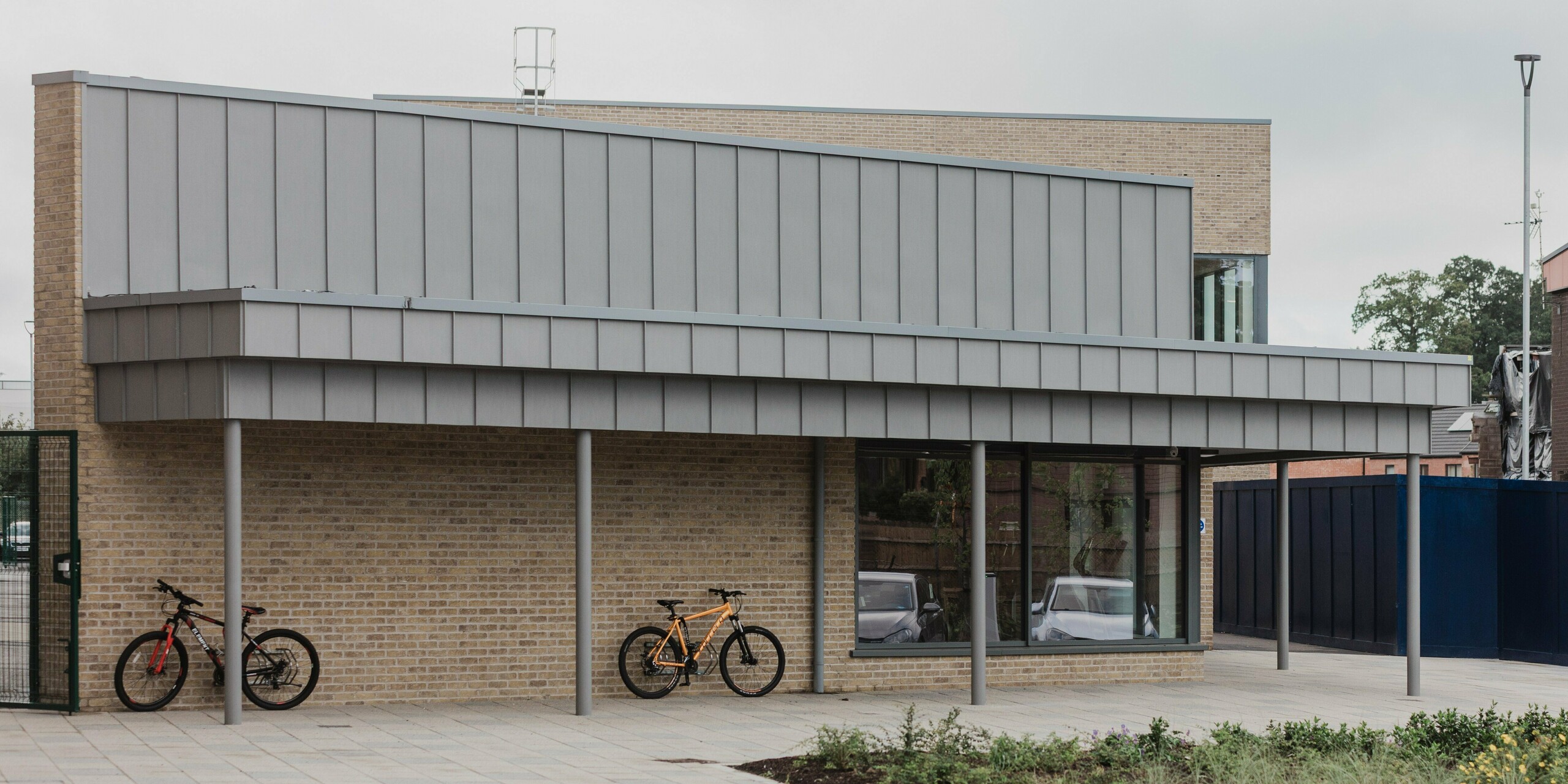 Northern Regional College in Ballymena features a modern bicycle shelter with a generous canopy made from PREFALZ standing seam cladding in patina grey. The vertically structured standing seam panels extend precisely over the roof edge, creating a striking feature above the clinker brick façade. Slender columns, light-coloured clinker walls, parked bicycles and the open forecourt emphasise the user-friendly character of the campus. PREFA aluminium impresses here with its durability, weather resistance and a calm, high-quality appearance in everyday use.