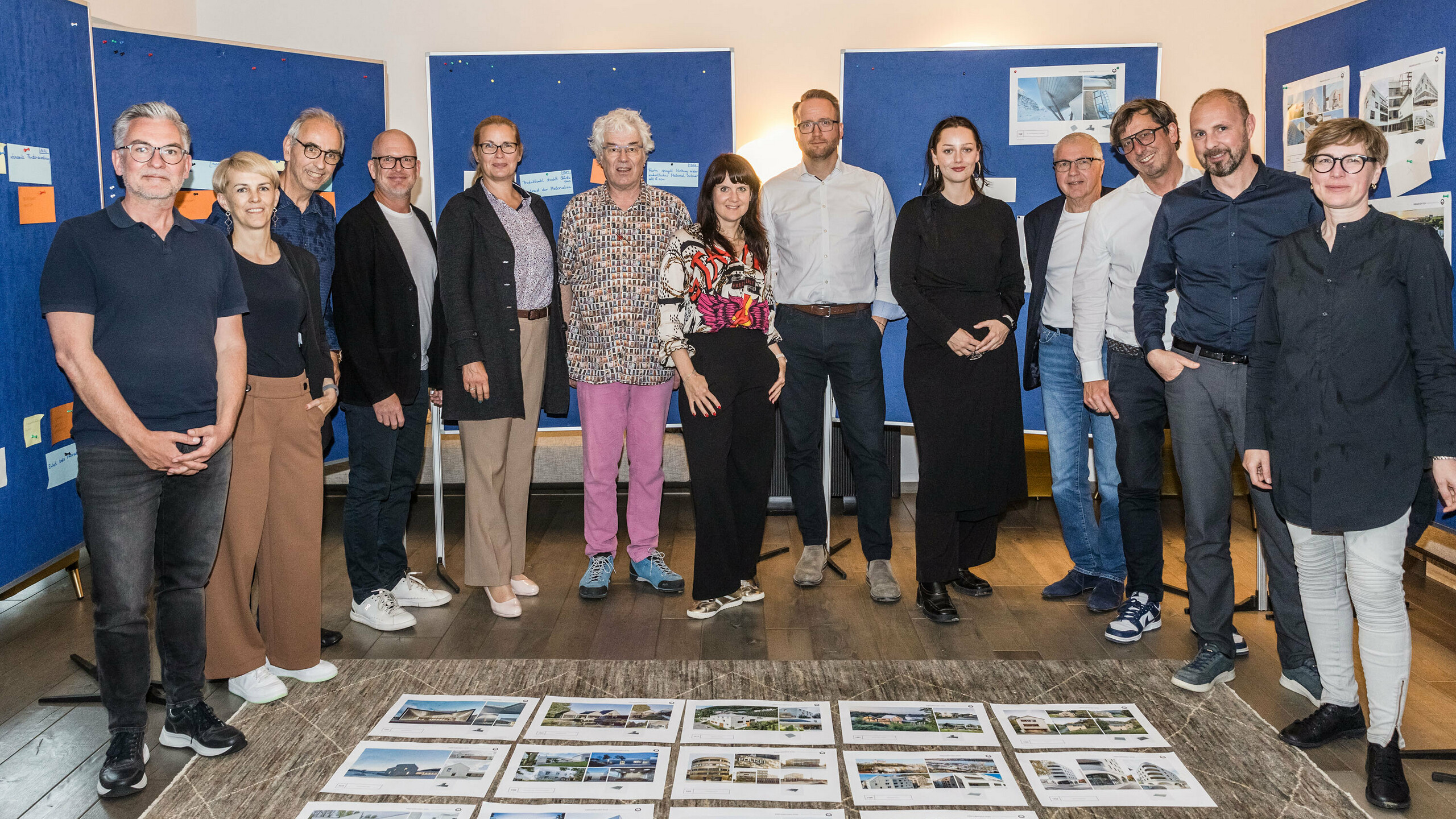 Group photo of the PREFARENZEN 2026 jury after the successful selection process in a winegrower's residence in Seewinkel, Burgenland: The interdisciplinary group of experts consisting of Dirk Lorenz (Leinert Lorenz Architekten), Veronika Roll (Marketing, PREFA Austria), Wolfgang Croce (Croce & Wir, Graz), Jürgen Jungmair (Head of International Marketing, PREFA), Judit Nemere (Managing Director, PREFA Hungary), Matthias Finkentey (Moderator), Bettina Almeida (Communications Management, PREFA), Christian Wirth (Regional Manager East, PREFA Austria), Selina Wach (Head of Discourse, Architektur Aktuell), Thomas Schlett (B3 Architekten), Sven Disser (Head of Development, Bauwerk), Falk Leinert (Leinert Lorenz Architekten) and Juliane Croce (Croce & Wir, Graz) stands in front of the final architectural projects selected for the PREFARENZEN architecture book and the 2026 calendar. The projects reflect diversity, sustainability and innovative use of PREFA materials.