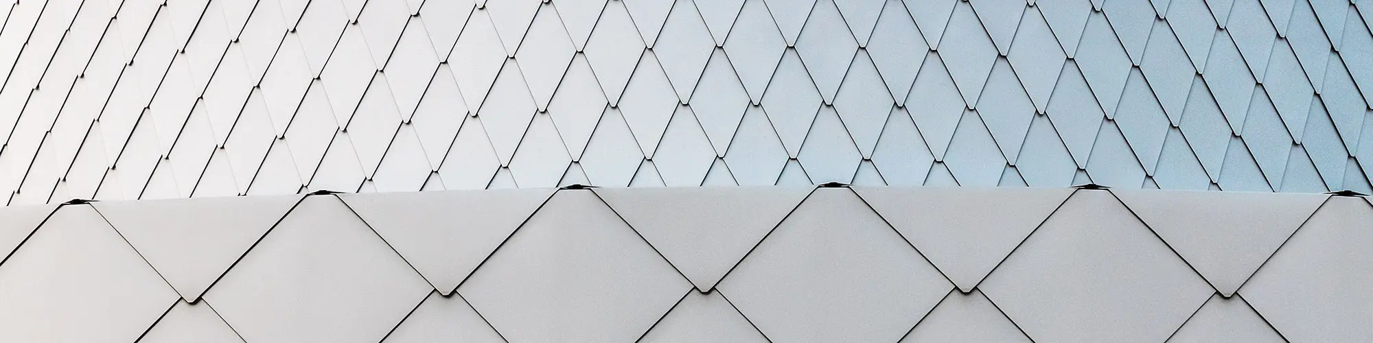 Close-up of the metallic silver façade made of PREFA rhomboid tiles that have been installed smoothly over the edges. The façade's flowing quality is clearly visible.