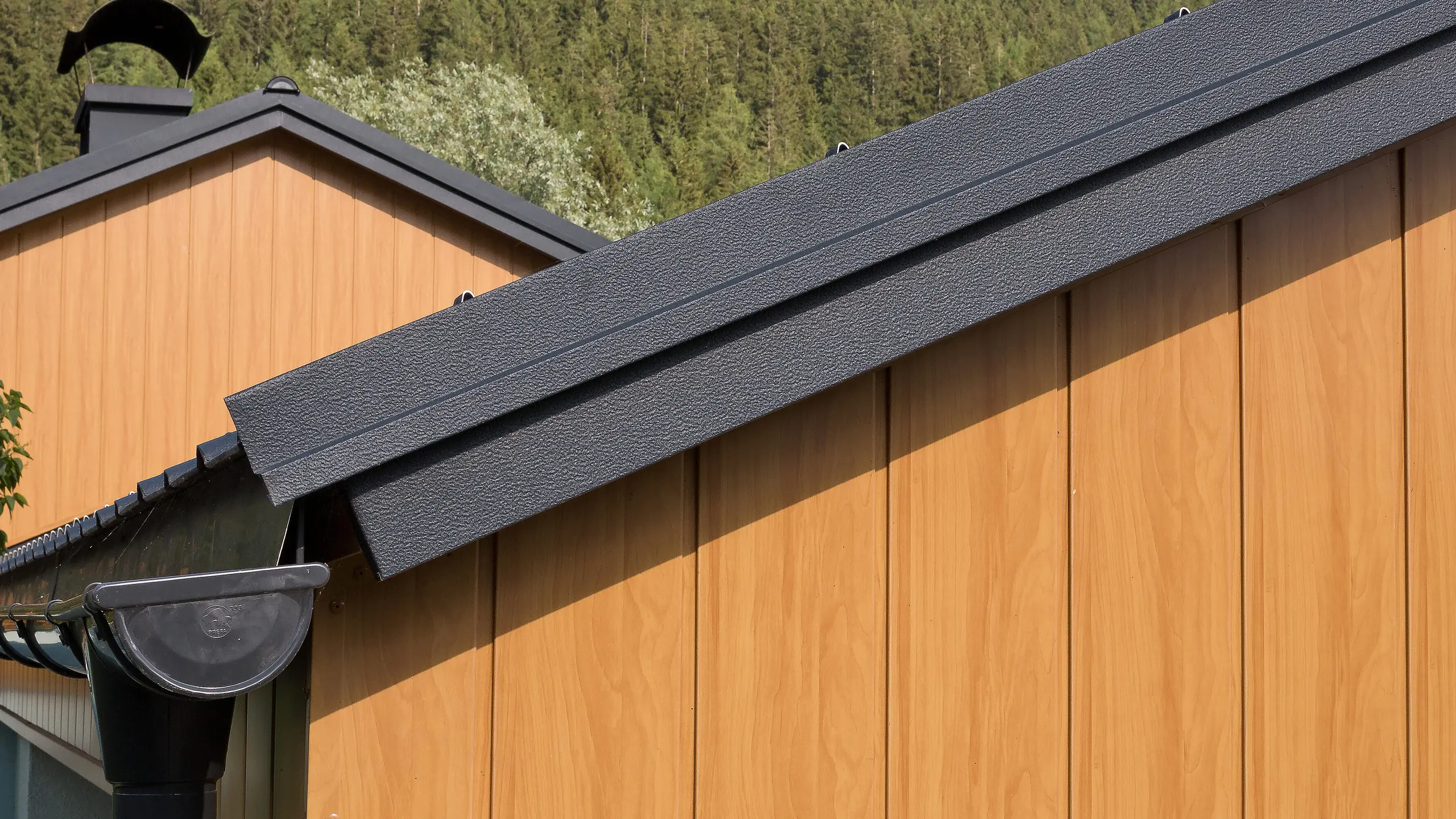 Gable cladding with aluminium sidings from PREFA in natural oak, installed vertically with a PREFA roof gutter in anthracite.