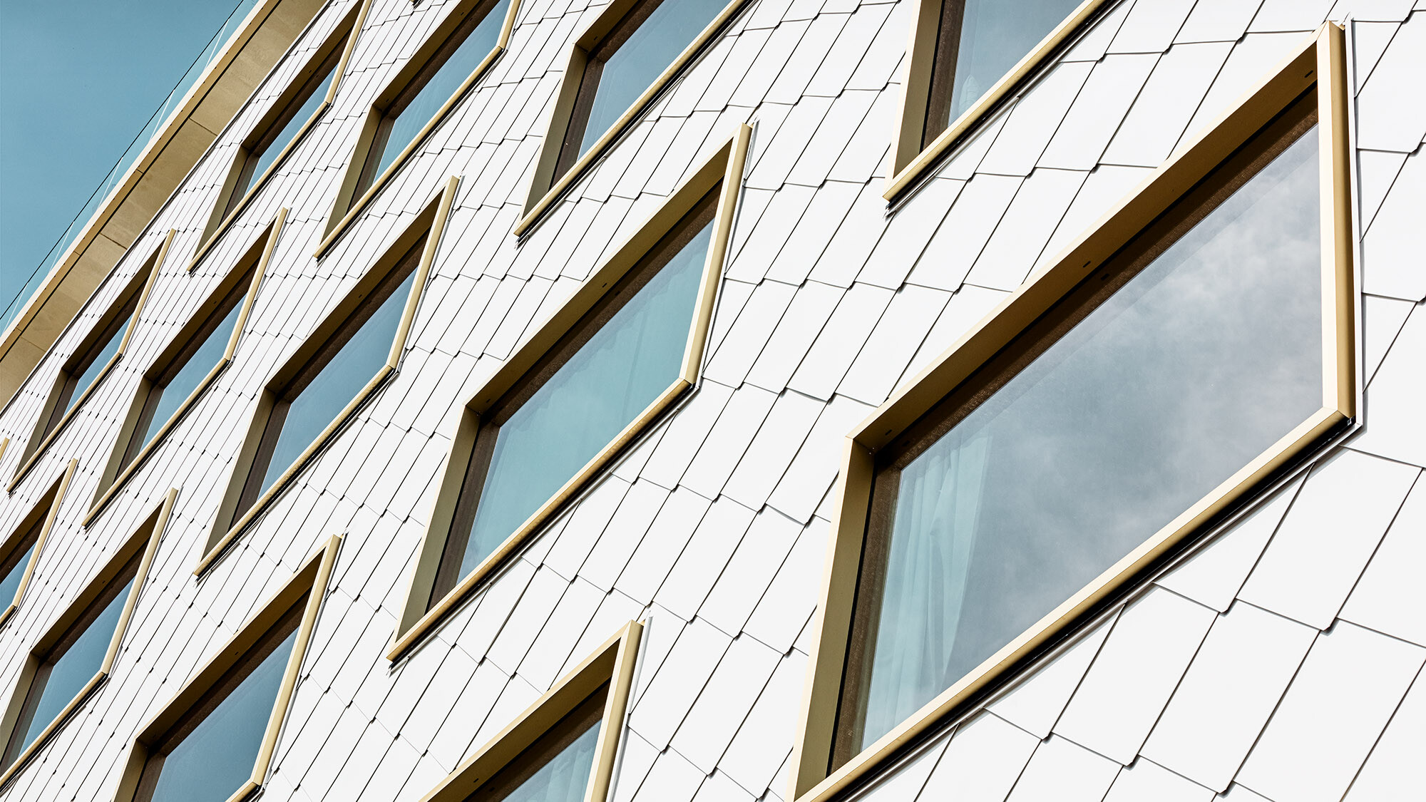 A close-up of the white rhomboid tile façade with the gold-framed windows from a worm's eye view.