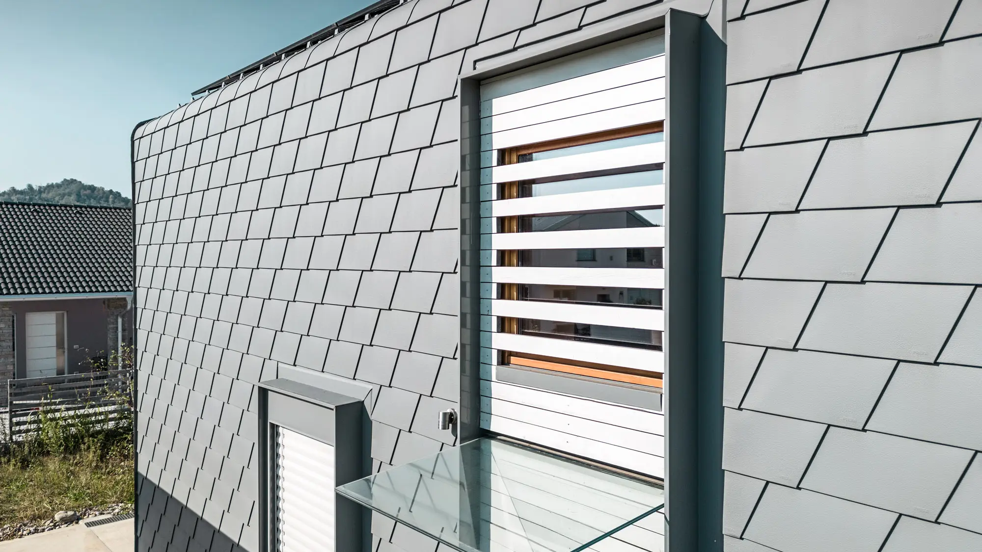 Detailed view of the façade with the accurately laid light-grey shingles.