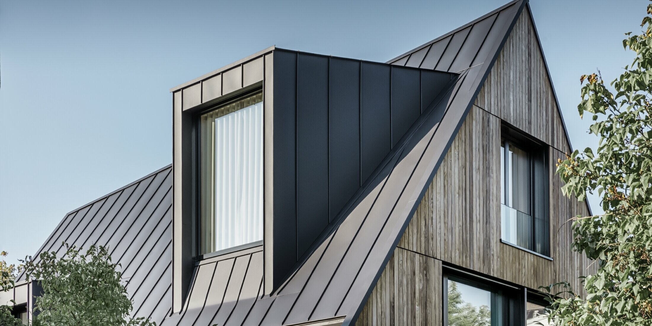 Steep gable roof with large dormer, covered with PREFALZ by PREFA in anthracite standing seam roof combined with wooden façade