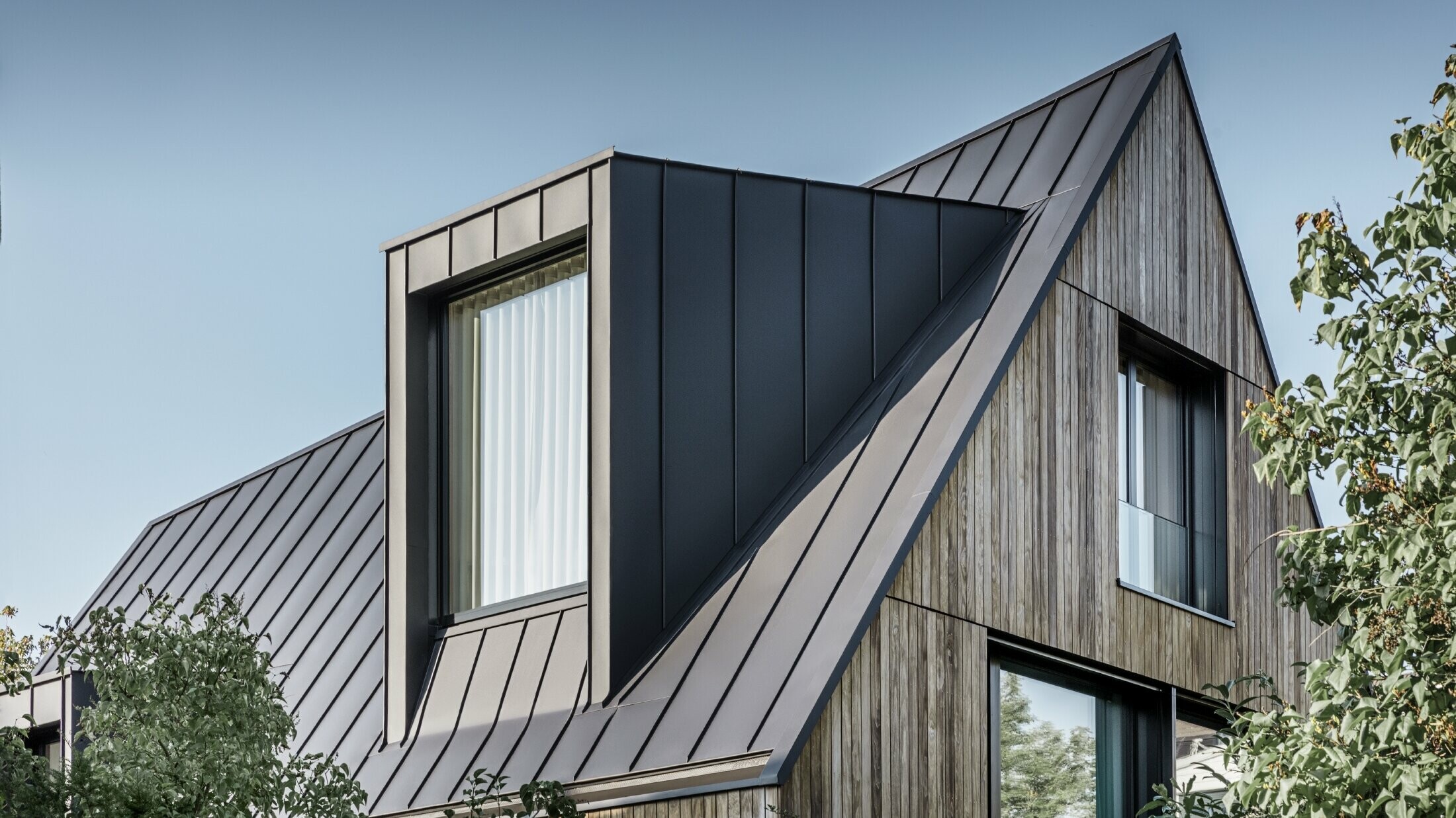 Steep gable roof with large dormer, covered with PREFALZ by PREFA in anthracite standing seam roof combined with wooden façade