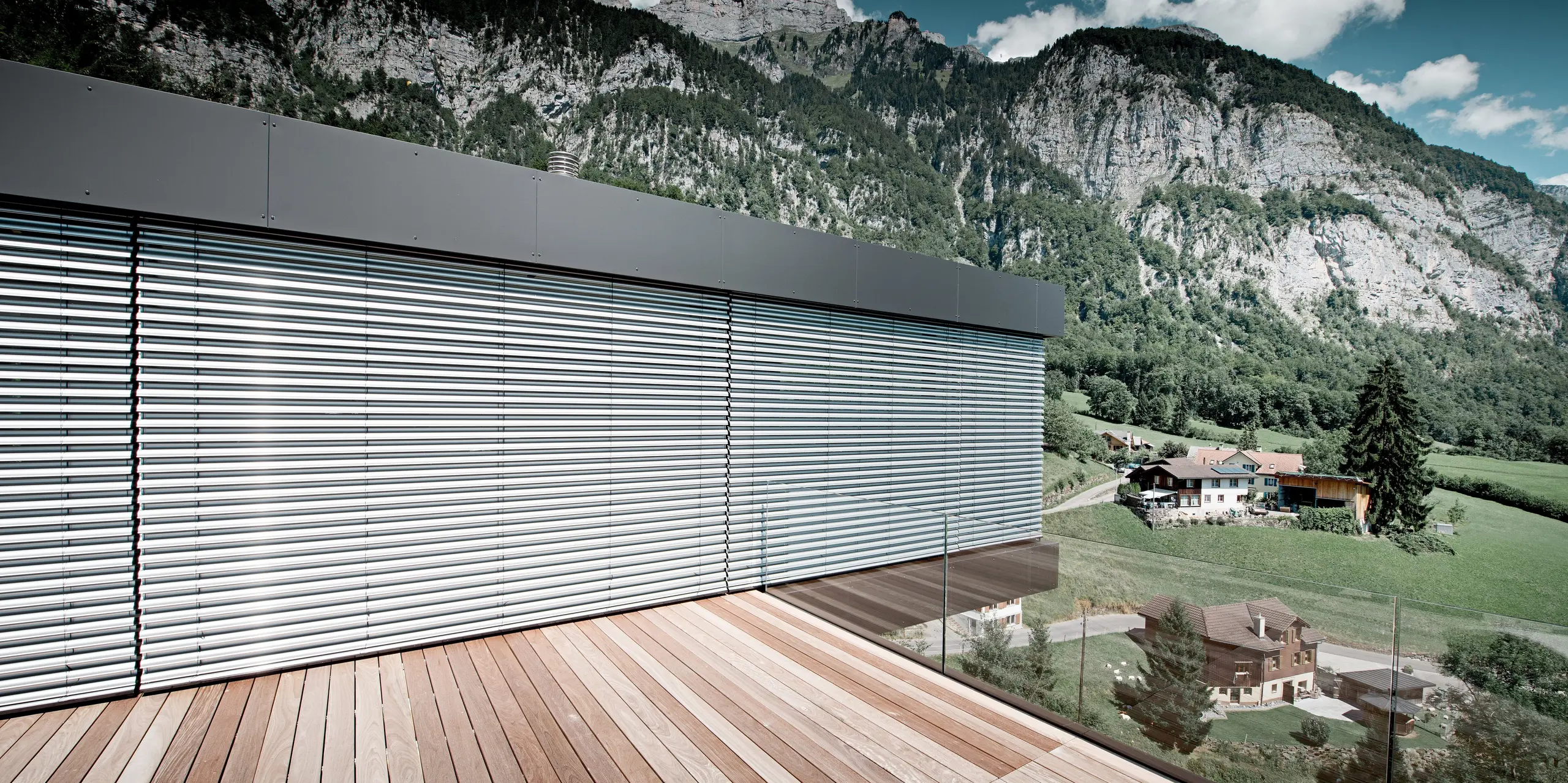 Großzügige Terrasse eines modernen Einfamilienhauses in Walenstadtberg mit atemberaubendem Blick auf die Schweizer Bergwelt. Die Fassade aus schwarzgrauen PREFA Aluminium Verbundplatten bildet einen markanten Kontrast zur Natur und unterstreicht die klare Architektur. Großflächige Verglasungen, elegante Linien und die langlebige, wartungsarme Aluminiumhülle sorgen für eine exklusive, zeitlose Ausstrahlung.