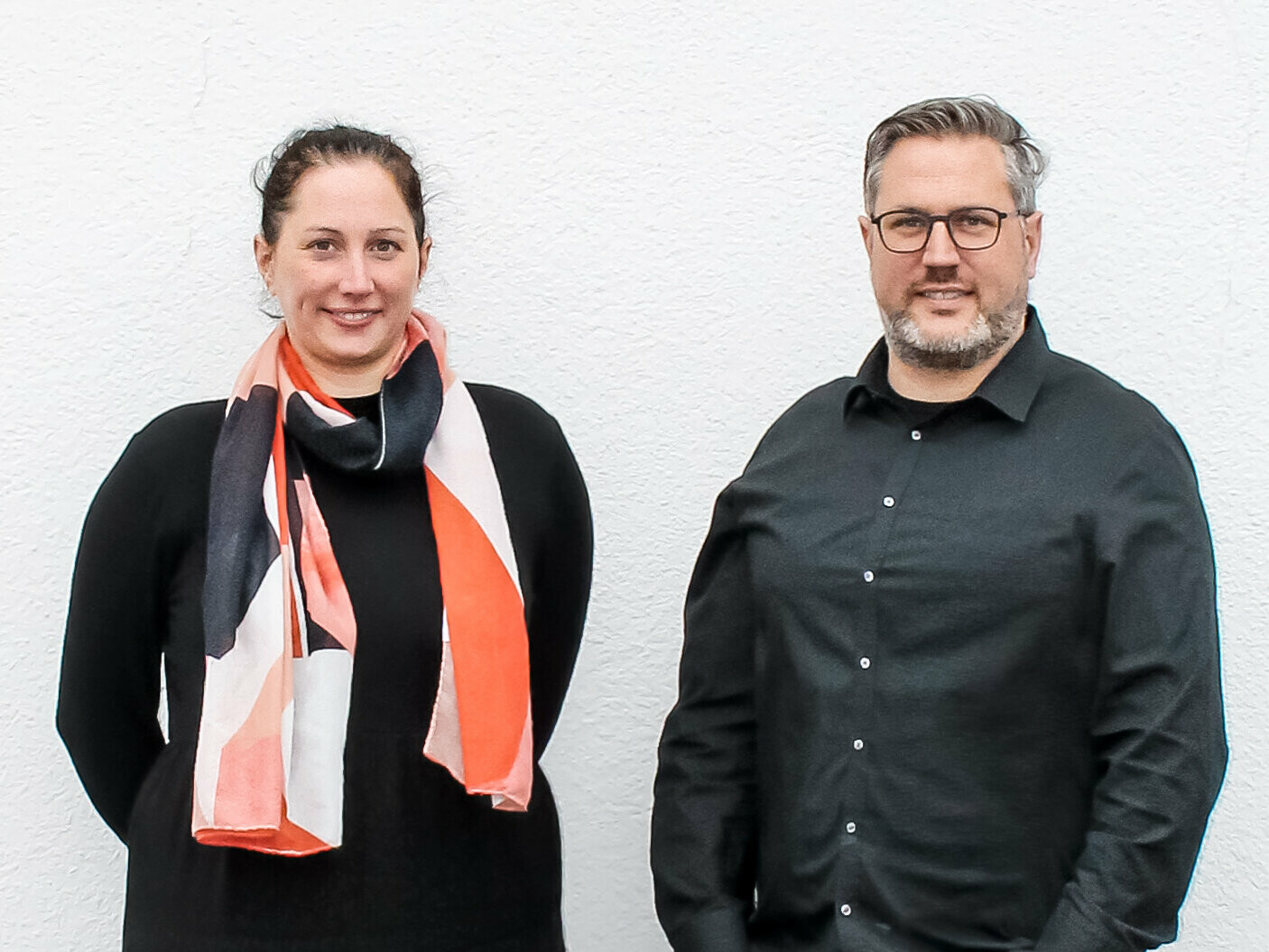 Portrait of the siblings Nathalie and Marc Bodarwé of BODARWE Architektur standing in front of a white plastered wall.