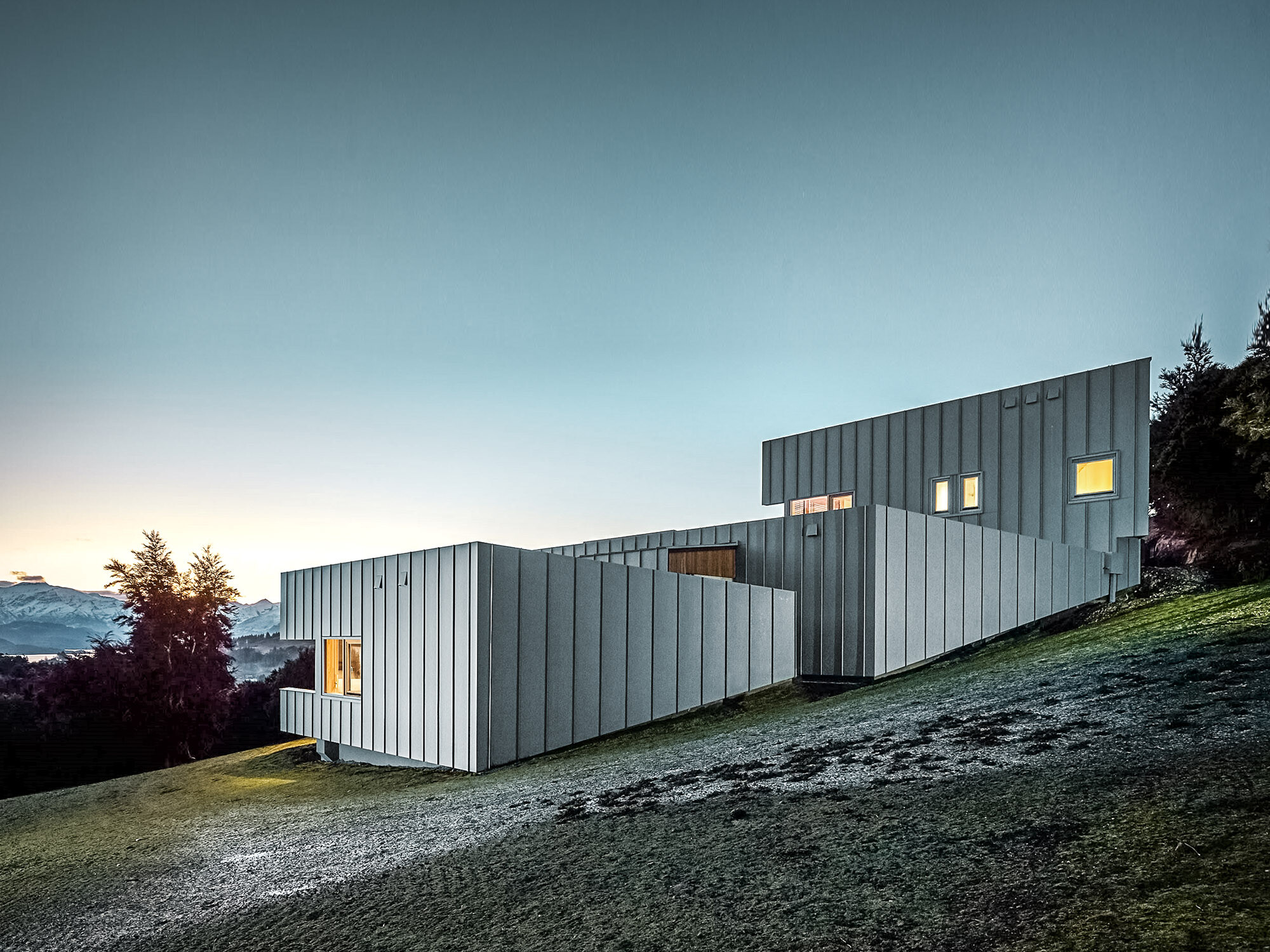 Evening shot of the building from the back: The house tucks into the hill, the landscape and the lake extending in front of it.