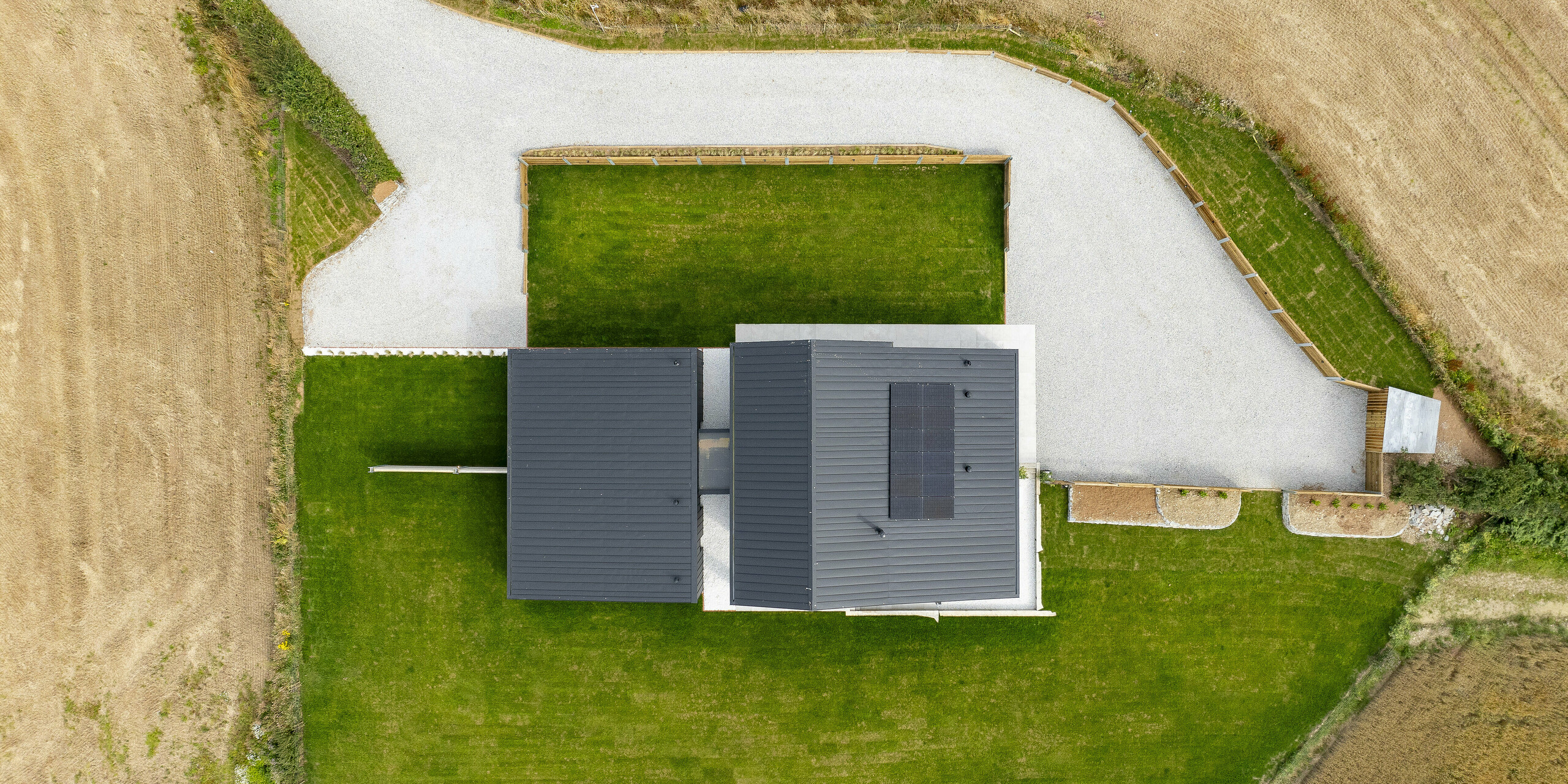 Aerial view of ‘The Hide’ in Cornwall, framed by well-kept meadows and wide fields. The aluminium roof made of PREFALZ in P.10 anthracite is characterised by clean lines and precise workmanship, combined with sustainable solar panels. The photovoltaic system provides electricity from sustainable renewable energy. The modern design blends harmoniously into the idyllic surroundings and offers an impressive bird's eye view.