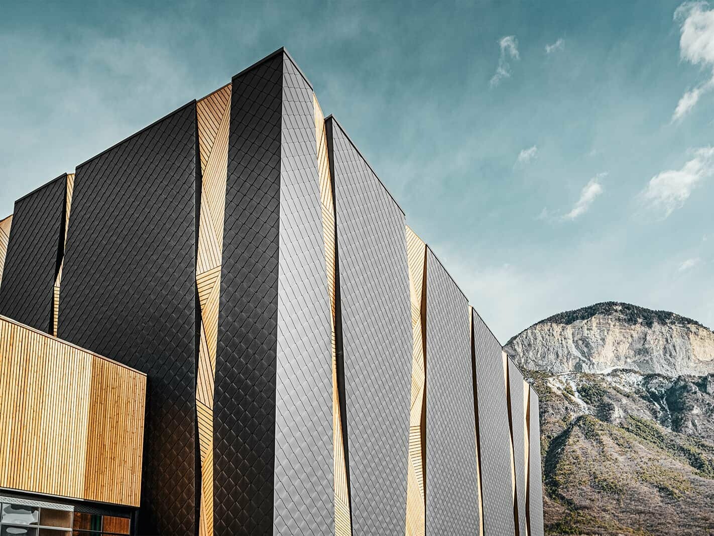 Rothoblaas industrial building with PREFA Rhomboid façade tile 44 × 44 in P.10 Black surrounded by a gigantic mountain backdrop.