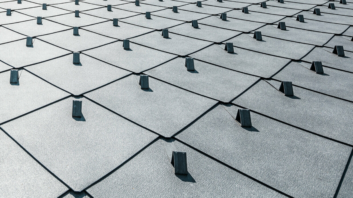 Detailed view of the PREFA rhomboid roof tile in the format 44 × 44 cm with a stucco surface in P.10 stone grey with snow guards