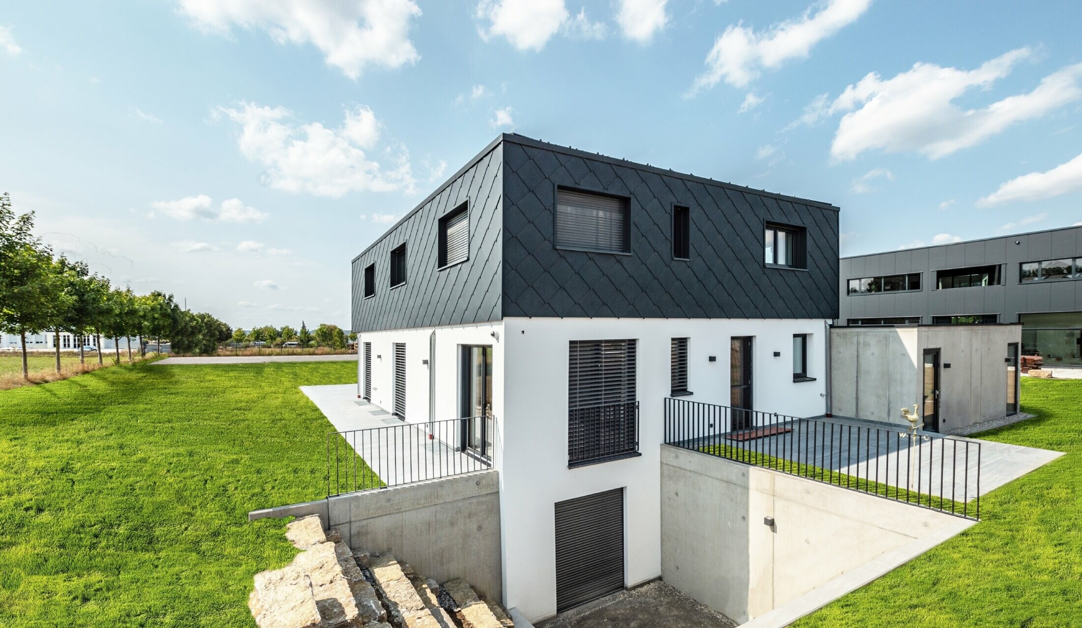 PREFA 44 x 44 rhomboid façade tile in anthracite with white rendered façade on a modest new build with flat roof.