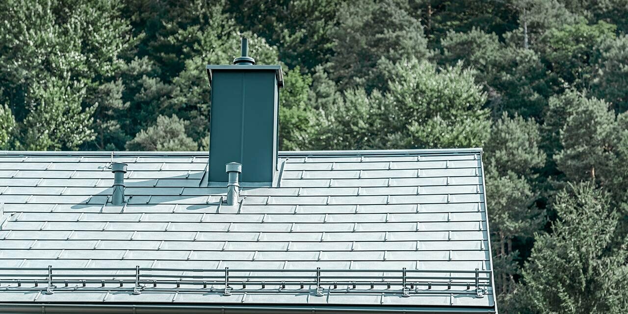 Detailed view of a gabled roof covered with the PREFA R.16 roof tile in stone grey with snow guard system, chimney surround, gutter and ventilation pipe also by PREFA