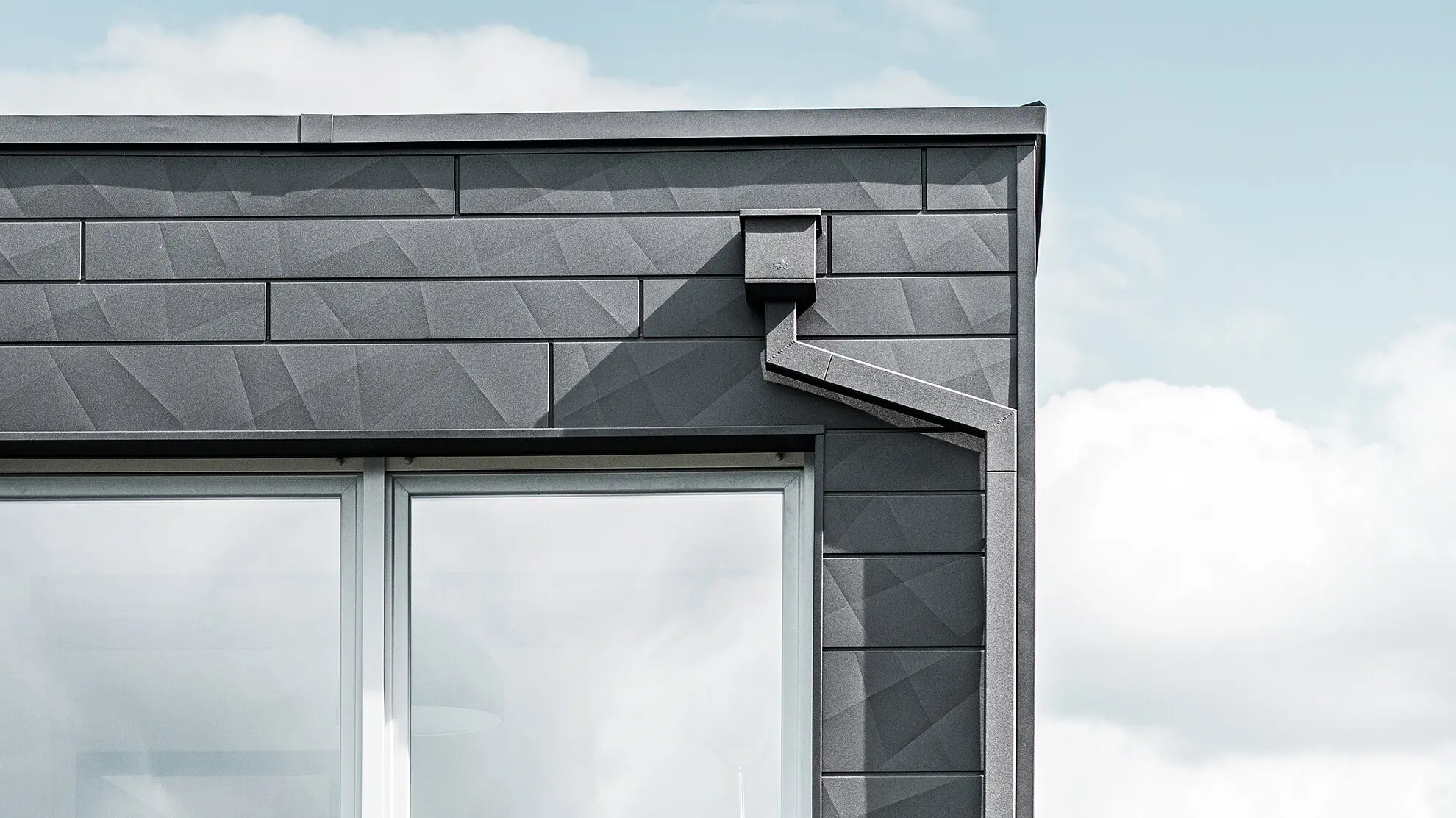 Gebäudeabschnitt eines modernen Einfamilienhauses mit Flachdach, die Entwässerung erfolgt mit dem hochwertigen PREFA Quadratrohr in Schwarz auf einer PREFA Siding.X Fassade.