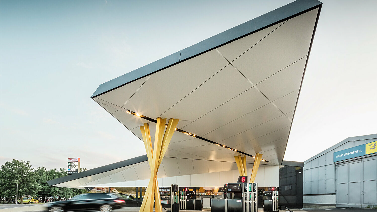 Side view of the petrol station with a bottom view of the roof, which rests on two groups of golden supports.
