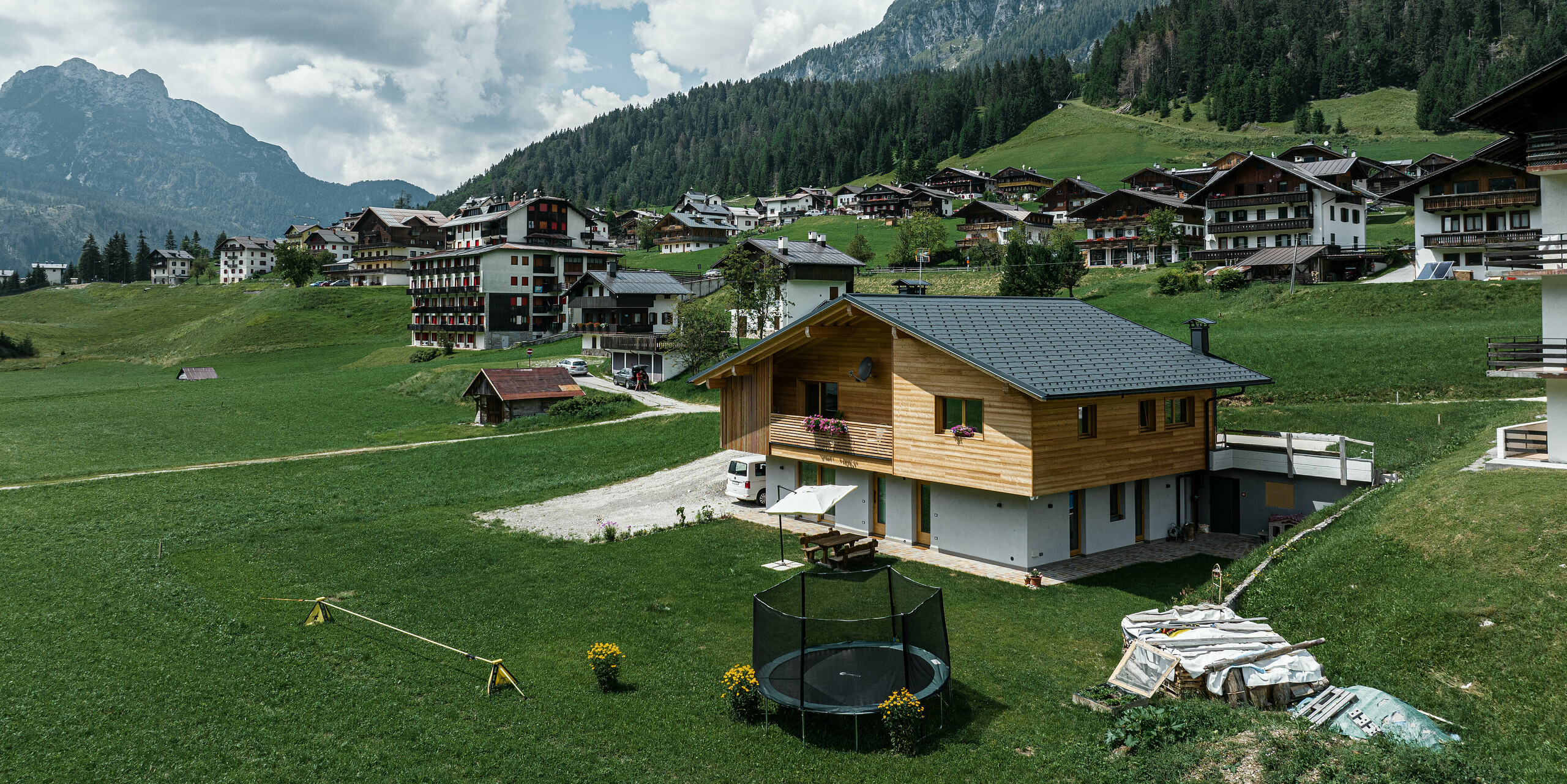 Casa Hoffe eingebettet in die malerische Berglandschaft Oberitaliens, verbindet regionale Bauweise mit modernen PREFA Aluminiumprodukten. Das Satteldach, gedeckt mit der Dachplatte R.16 in P.10 Schwarz, bietet einen zeitlosen Schutz und Kontrast zur klassischen Holzfassade. Die Fassadenpaneele Siding.X ergänzen den Eingangsbereich des Einfamilienhauses, während die umliegenden Berge und grünen Wiesen das naturintegrierte Konzept unterstreichen.