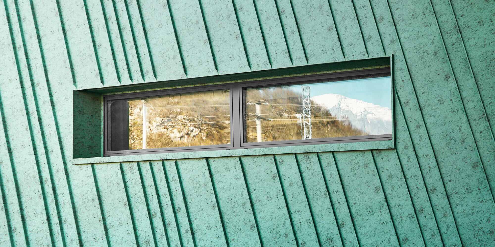 Detail with slightly slanted façade and a small, elongated window that reflects the mountains and electrical lines. Lateral view of the façade and glass front with an entrance. 