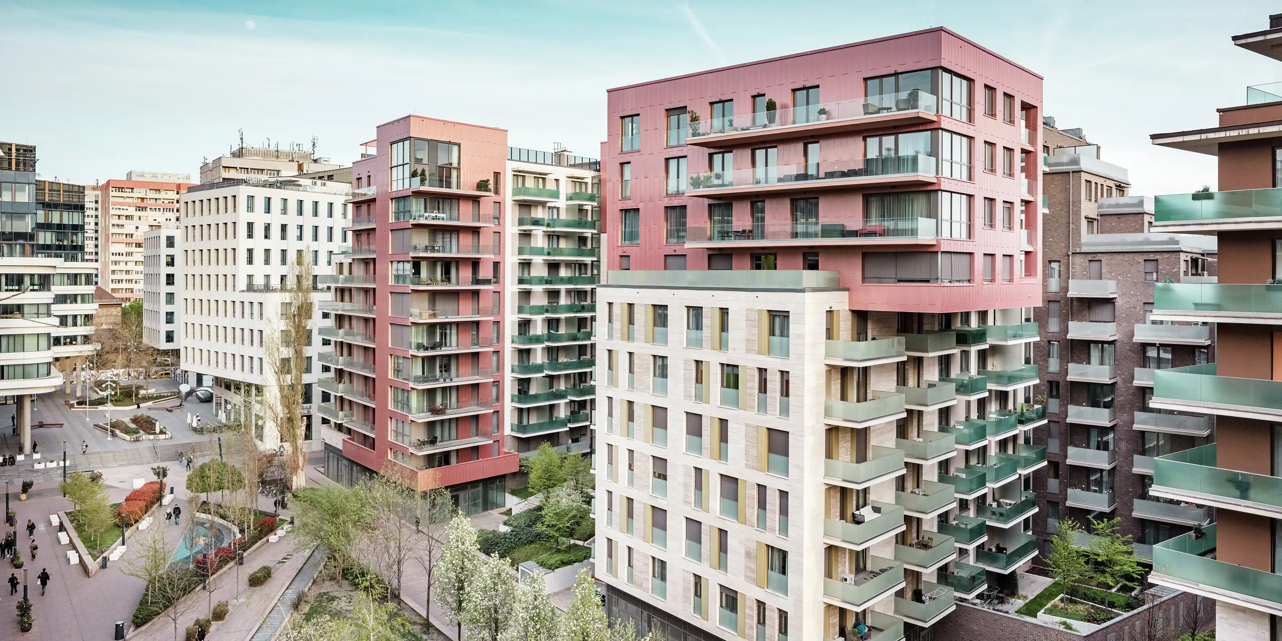 Stimmungsvolle Gesamtansicht des Grand Corvin Ensembles im Budapester Corvin-Viertel. Die markanten Obergeschosse sind mit PREFA Siding Fassadenpaneelen in vertikaler Verlegung und Sonderfarbe Lachsmetallic gestaltet. In Kombination mit Naturstein und großzügigen Glasflächen entsteht ein modernes, hochwertiges Stadtbild. Die langlebige Aluminiumfassade betont die architektonische Vielfalt und den nachhaltigen Anspruch der umfassenden Stadterneuerung.