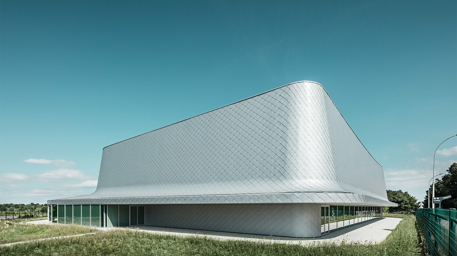 Side view of the hall surrounded by grass and a path. The glazing is partially visible.