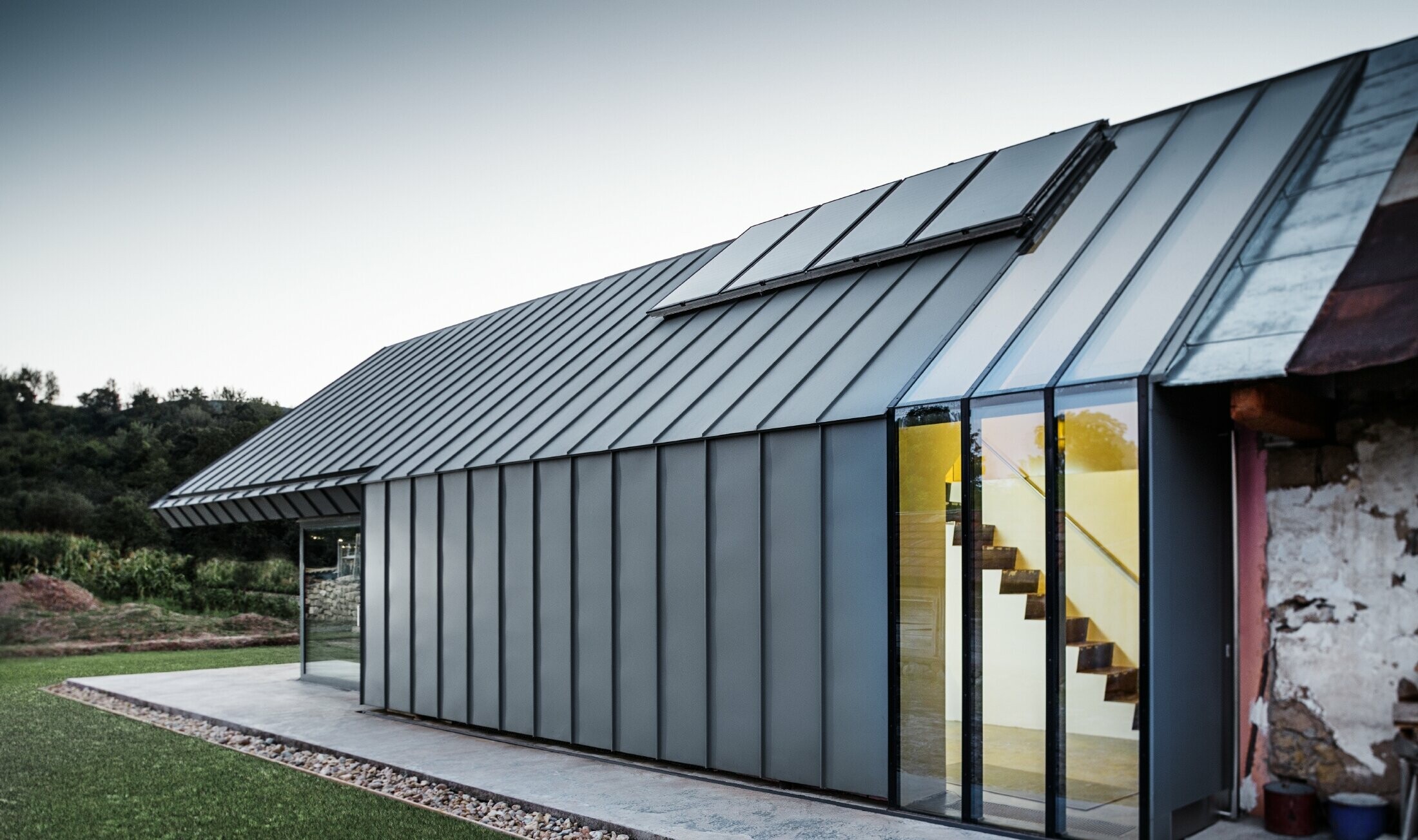 Modern architect’s office and detached house adjoining an old farmhouse with a stone façade, clad in PREFA standing seam and single lock standing seam in light grey