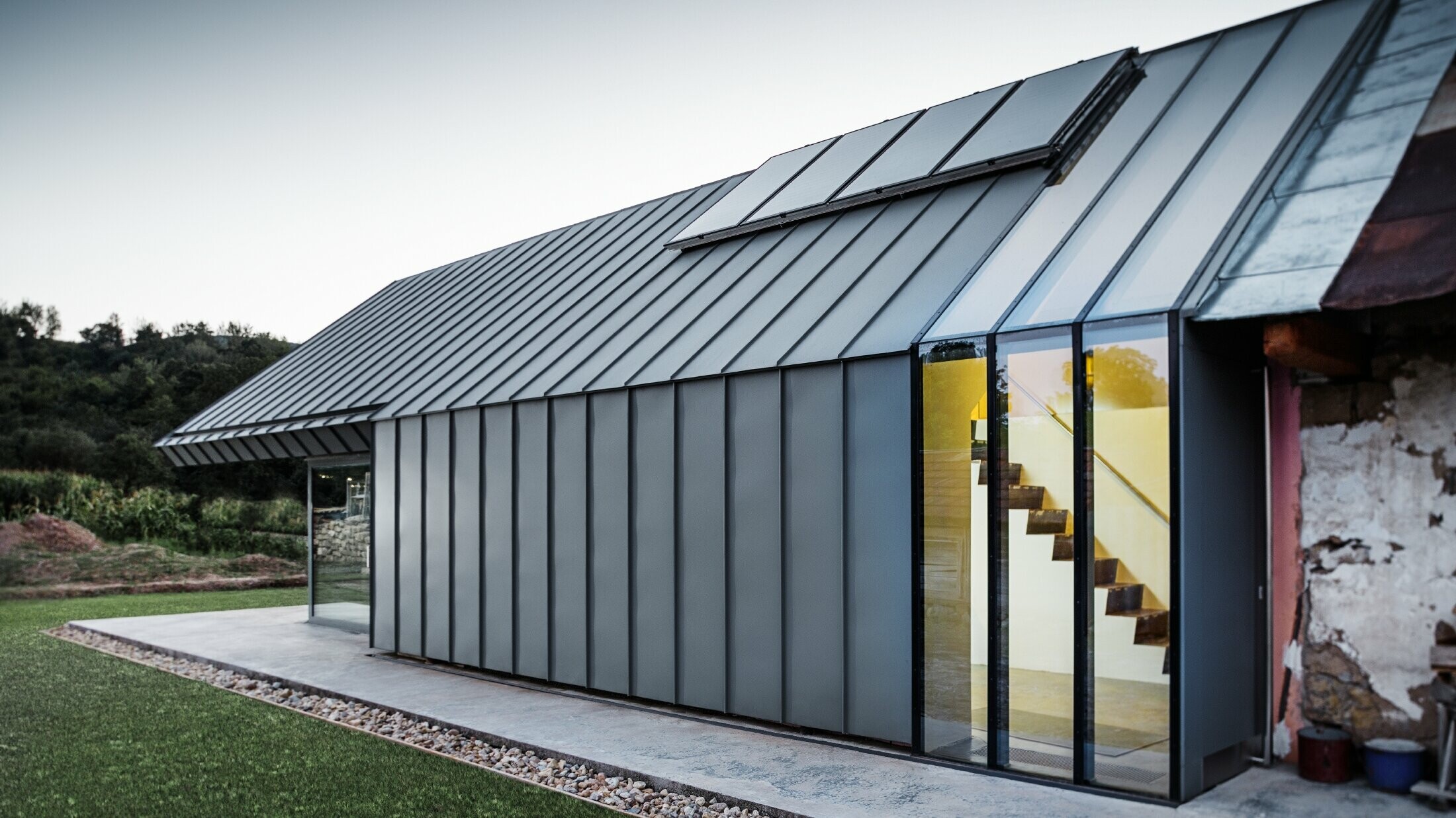 Modern architect’s office and detached house adjoining an old farmhouse with a stone façade, clad in PREFA standing seam and single lock standing seam in light grey