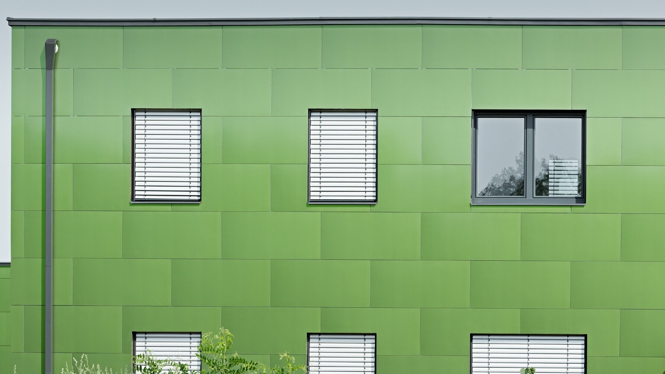 Frontal view of the PREFA aluminium composite panel with chameleon look and changing colours. On the far left, you can see the PREFA square downpipe