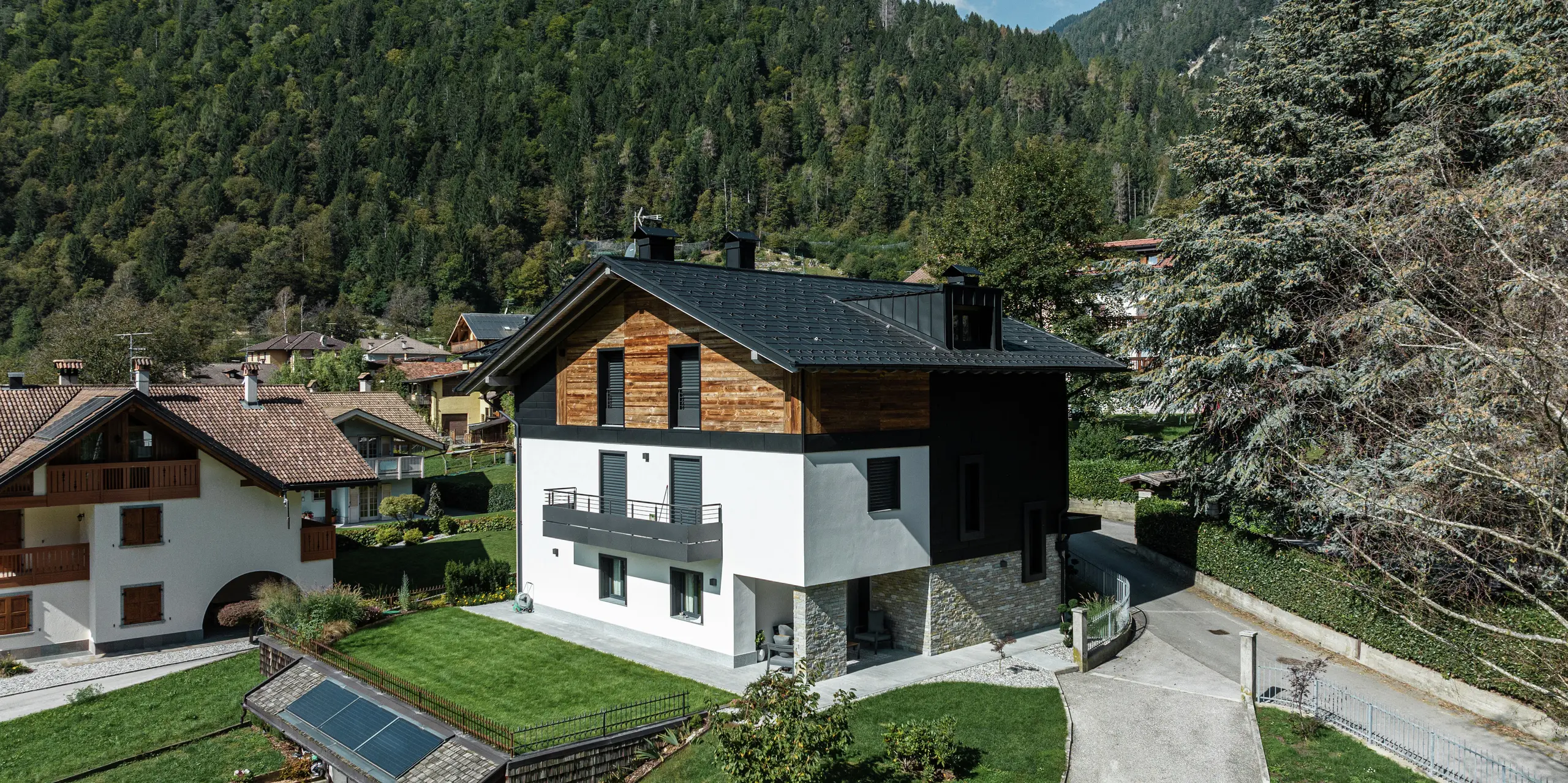 Modernes Wohnhaus in Pelugo, Italien, nach Renovierung und energetischer Sanierung. Das Dach wurde mit der widerstandsfähigen PREFA Dachplatte R.16 in P.10 Anthrazit eingedeckt, die Fassade erhielt mit PREFA Siding.X in P.10 Anthrazit eine moderne und langlebige Optik. Die Kombination von Aluminium, Holz und Putz schafft eine harmonische und witterungsbeständige Architektur.