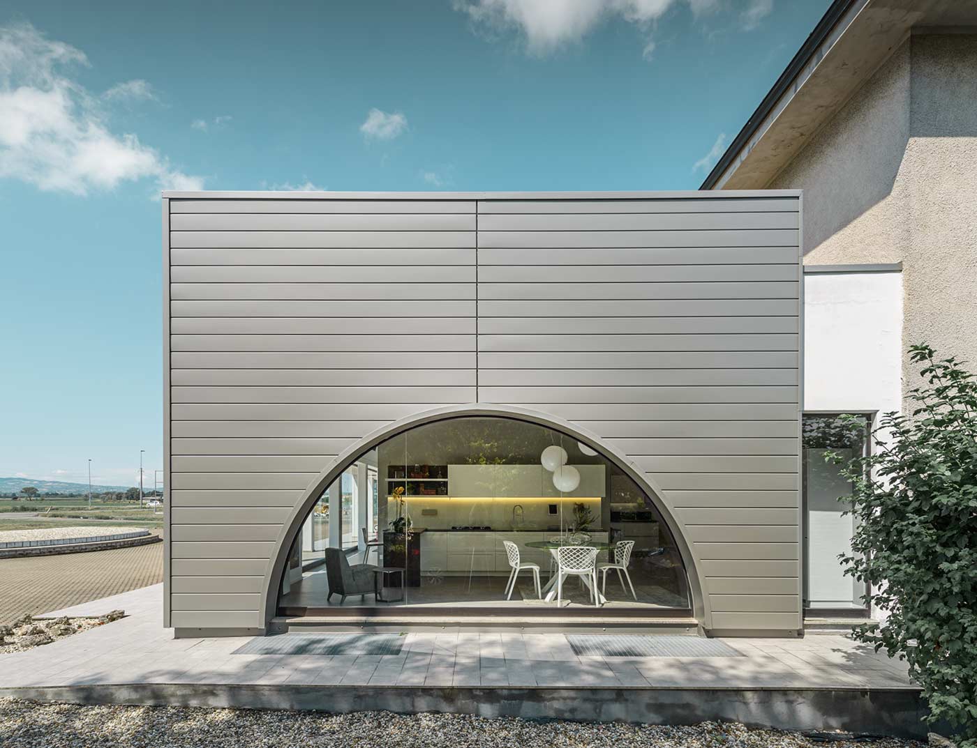 Flat-roof extension with a curved window façade, the façade is clad with horizontal aluminium panels, the PREFA sidings in smoke silver.