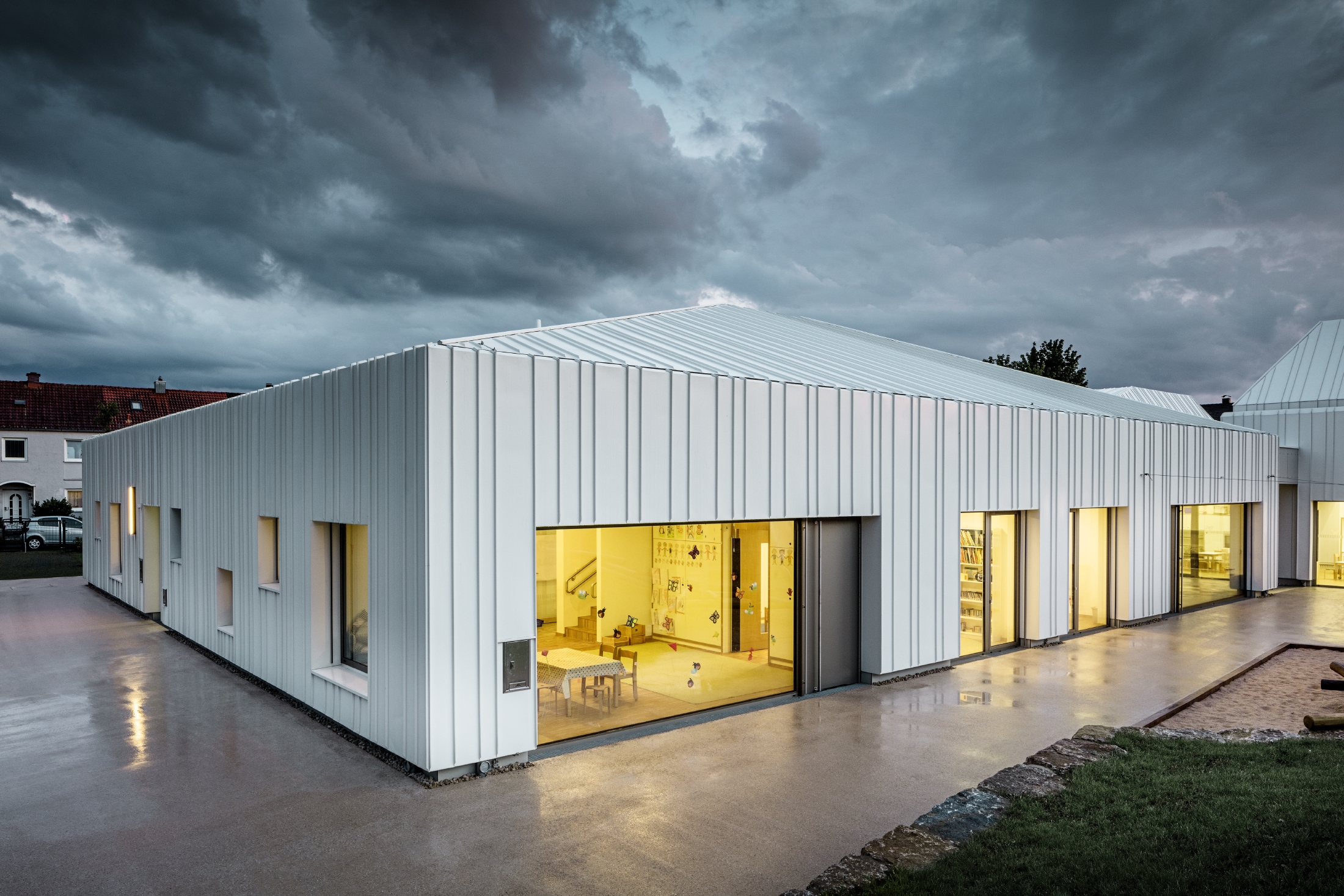 Day nursery in Niederwerrn with PREFALZ roof and façade in pure white with different widths of panels photographed at dusk and in a cloudy atmosphere
